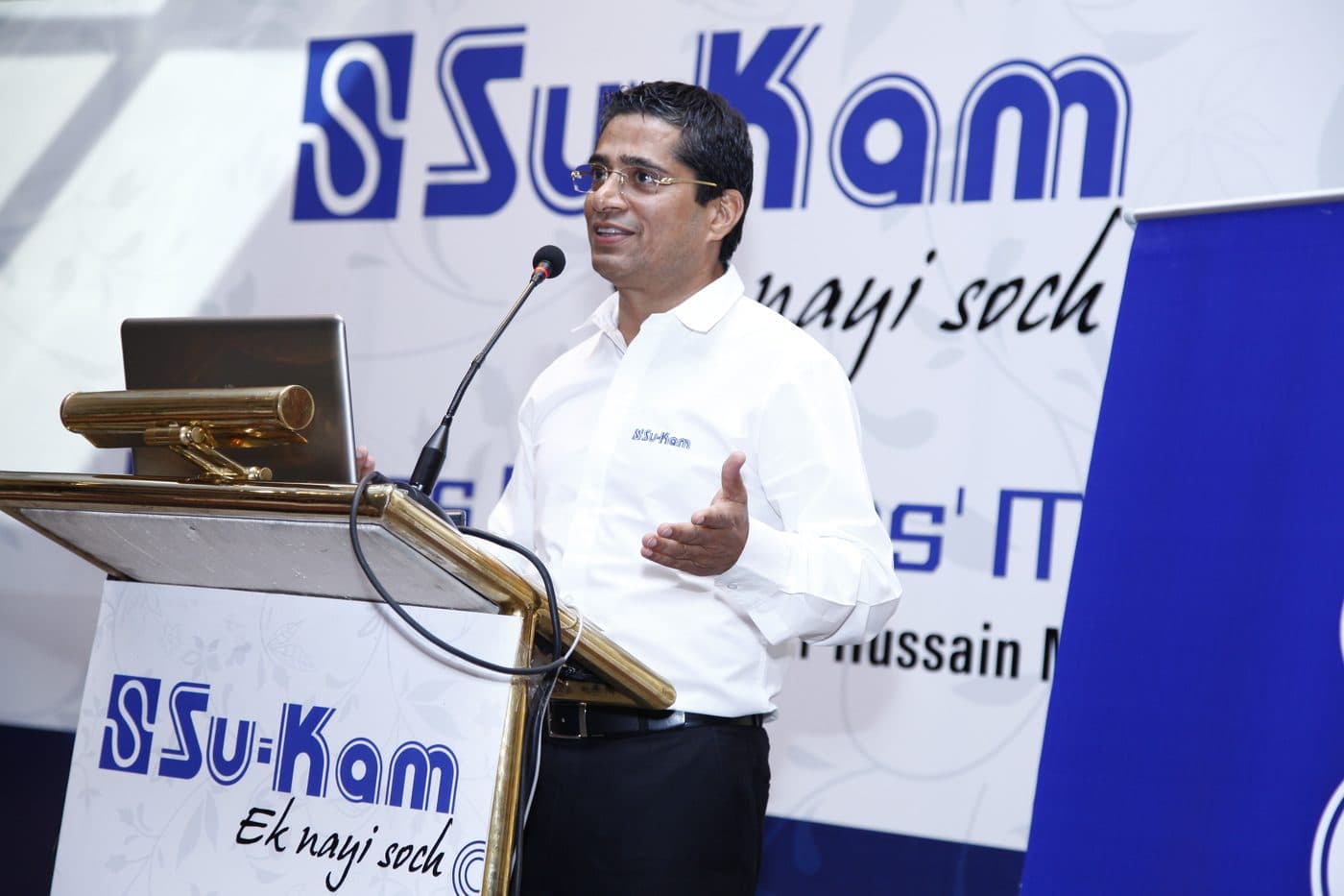 Kunwer Sachdev speaking at a podium during the Su-Kam years
